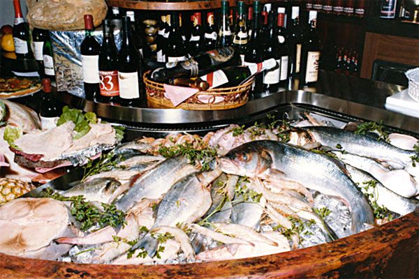 Pesce fresco in esposizione sul ghiaccio, con le bottiglie di vino sullo sfondo